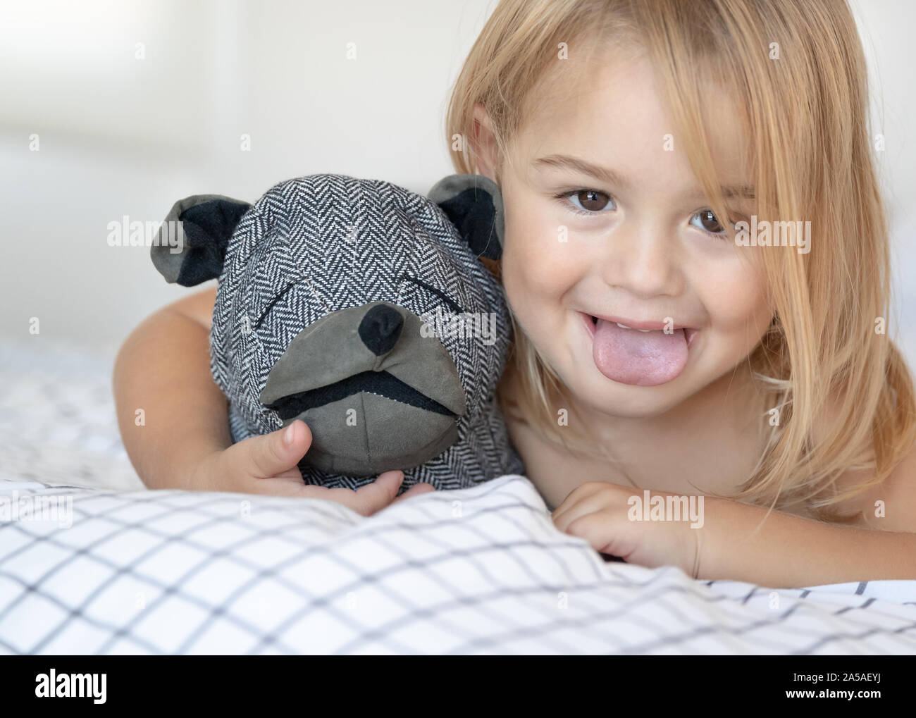 Baby il divertimento a casa closeup ritratto di un simpatico ragazzino rendendo volti, che mostra la linguetta, giocando con soft cane giocattolo, felice infanzia sani Foto Stock