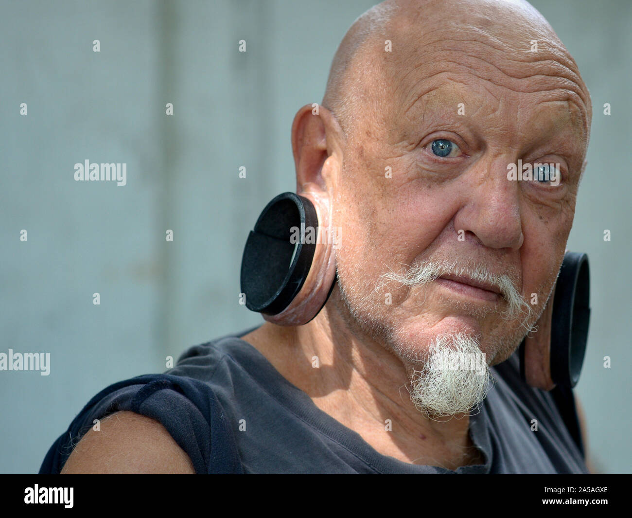 Anziani uomo caucasico (expat) con enormi orecchioni allungato pone per la fotocamera. Foto Stock