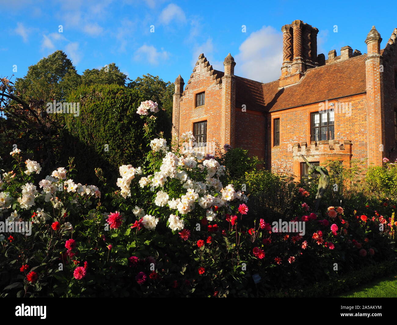 Chenies Manor House rivolta ad ovest.il bel tempo, cielo blu e in cotto antico al sole con colouful dalie, Cosmos e rose in piena fioritura. Foto Stock