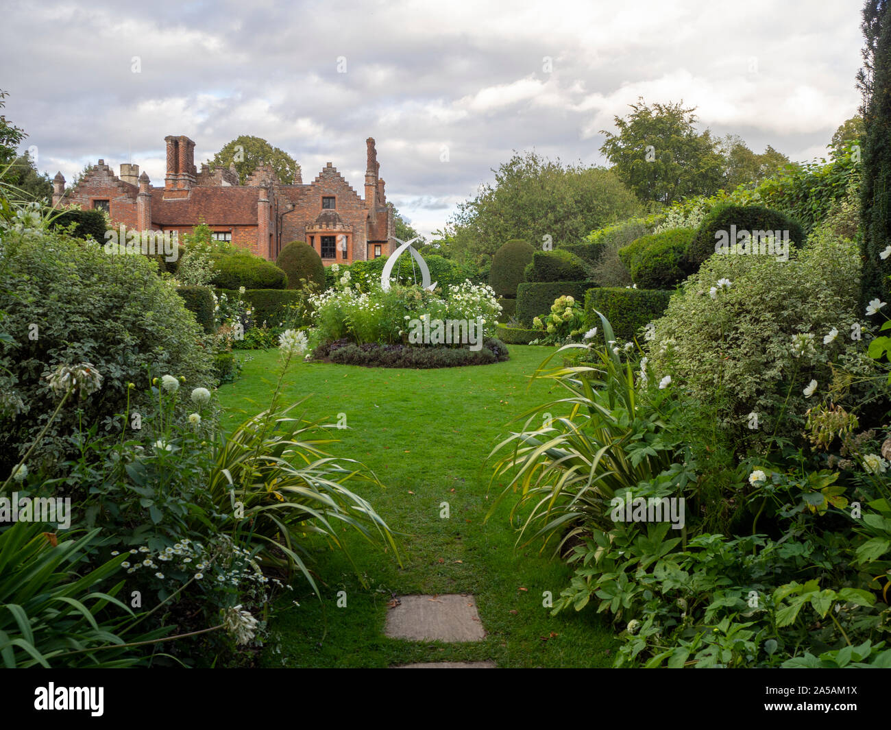 Chenies Manor da topiaria da giardino con featured scultura, impianti frontiere, tonalità di verde delle foglie e fiori di colore bianco. Foto Stock