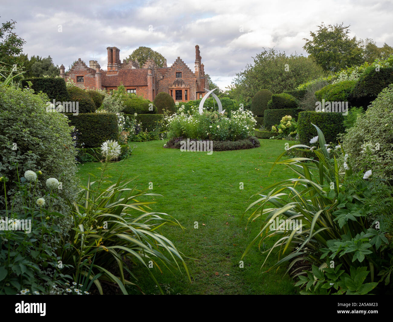 Chenies Manor da topiaria da giardino con featured scultura, impianti frontiere, tonalità di verde delle foglie e fiori di colore bianco. Foto Stock