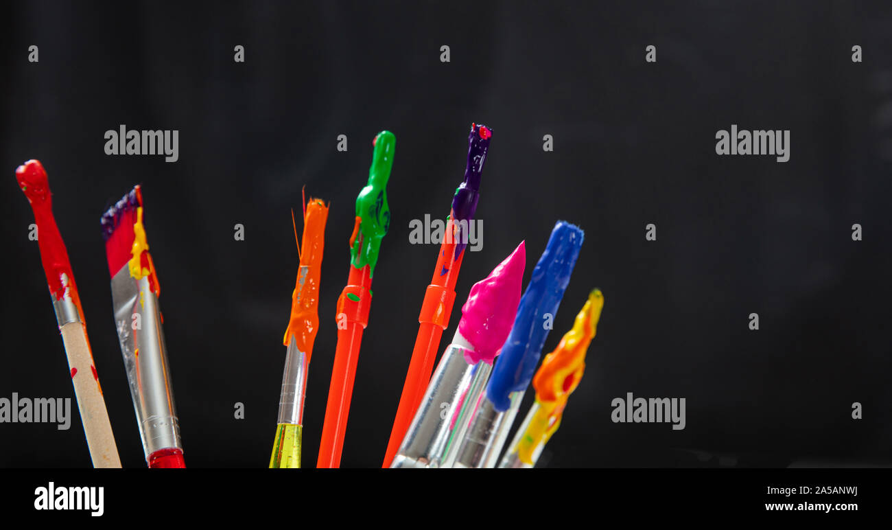 Il concetto di pittura. Pennelli con vernici colorate su nero colore di sfondo e primo piano, spazio di copia Foto Stock