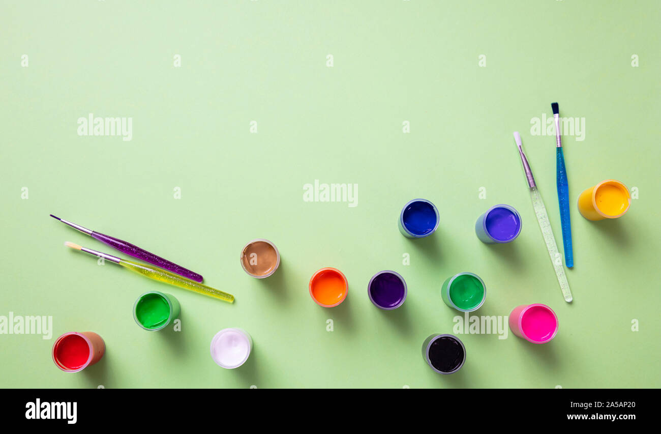 I bambini la creatività. Dito colorati vernici e set di pennelli per dipingere sul verde pastello colore di sfondo, vista dall'alto, spazio di copia Foto Stock