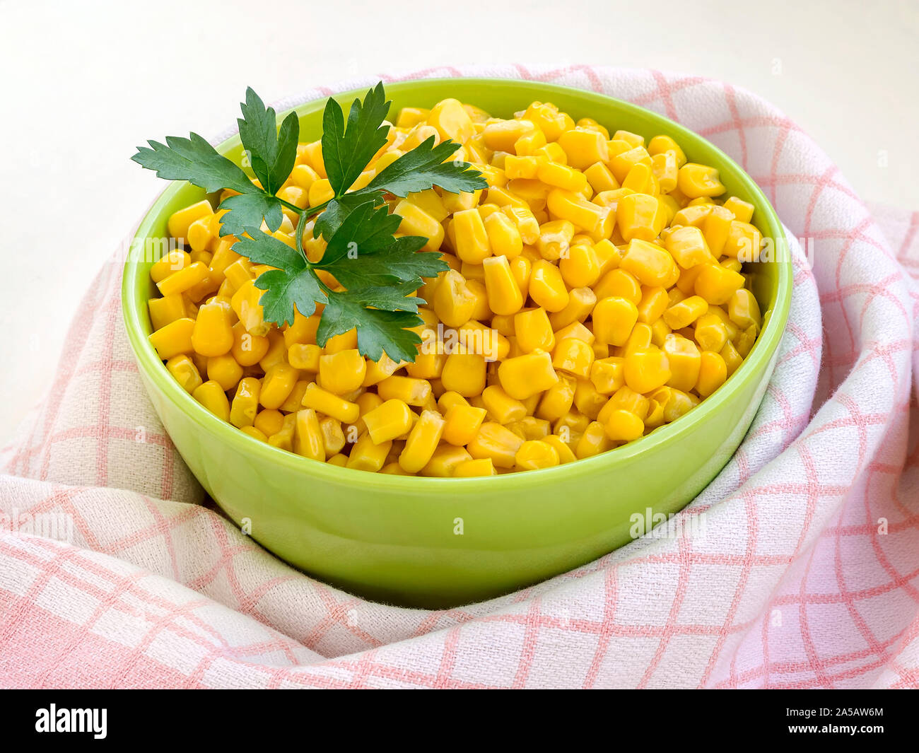 Close-up di conserve di mais dolce in una ciotola verde vicino a scacchi asciugamano da cucina. Guarnire e ingrediente per insalate. Cibo vegetariano. Vista laterale. Foto Stock