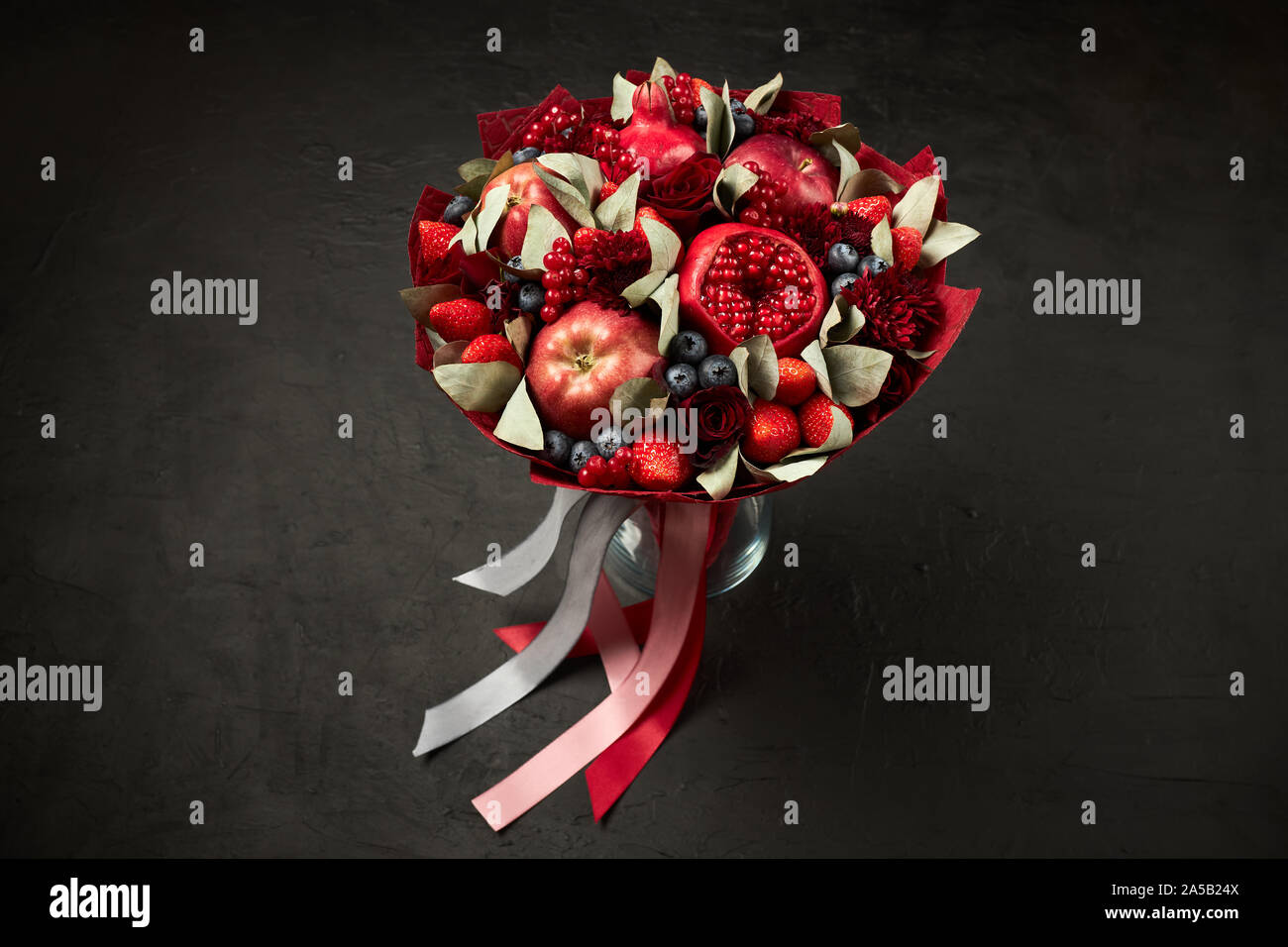 Composizione unica nella forma di un bouquet di melograni, mele, fragole, ribes rosso e rose su sfondo nero Foto Stock