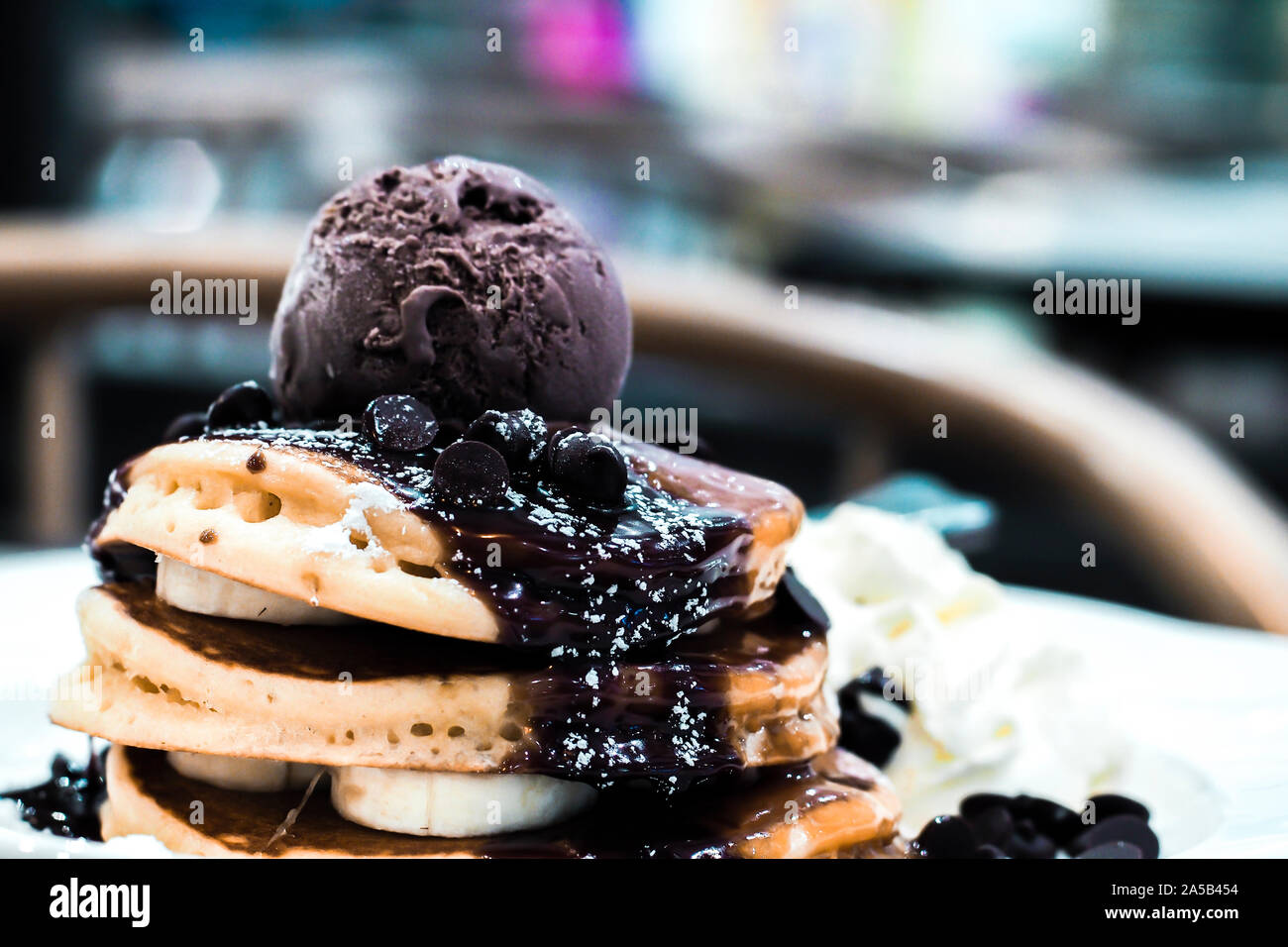 Un bicchierino ravvicinato di decadenti pancake al latte a strati di banane affettate, ricco sciroppo di cioccolato, gocce di cioccolato e gelato. Foto Stock