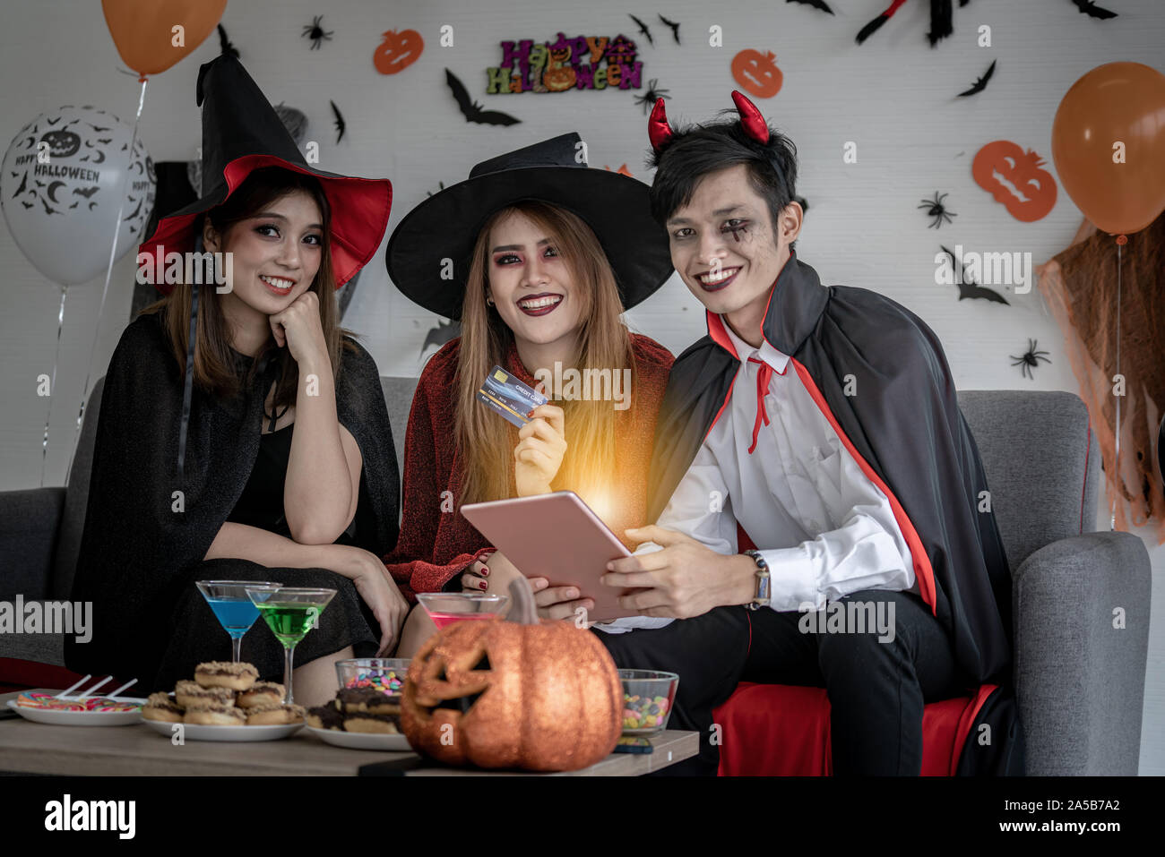 Un gruppo di giovani e di adulti di adolescente persone celebrare una festa di Halloween festa di carnevale in costume di Halloween e facendo shopping online con la compressa Foto Stock
