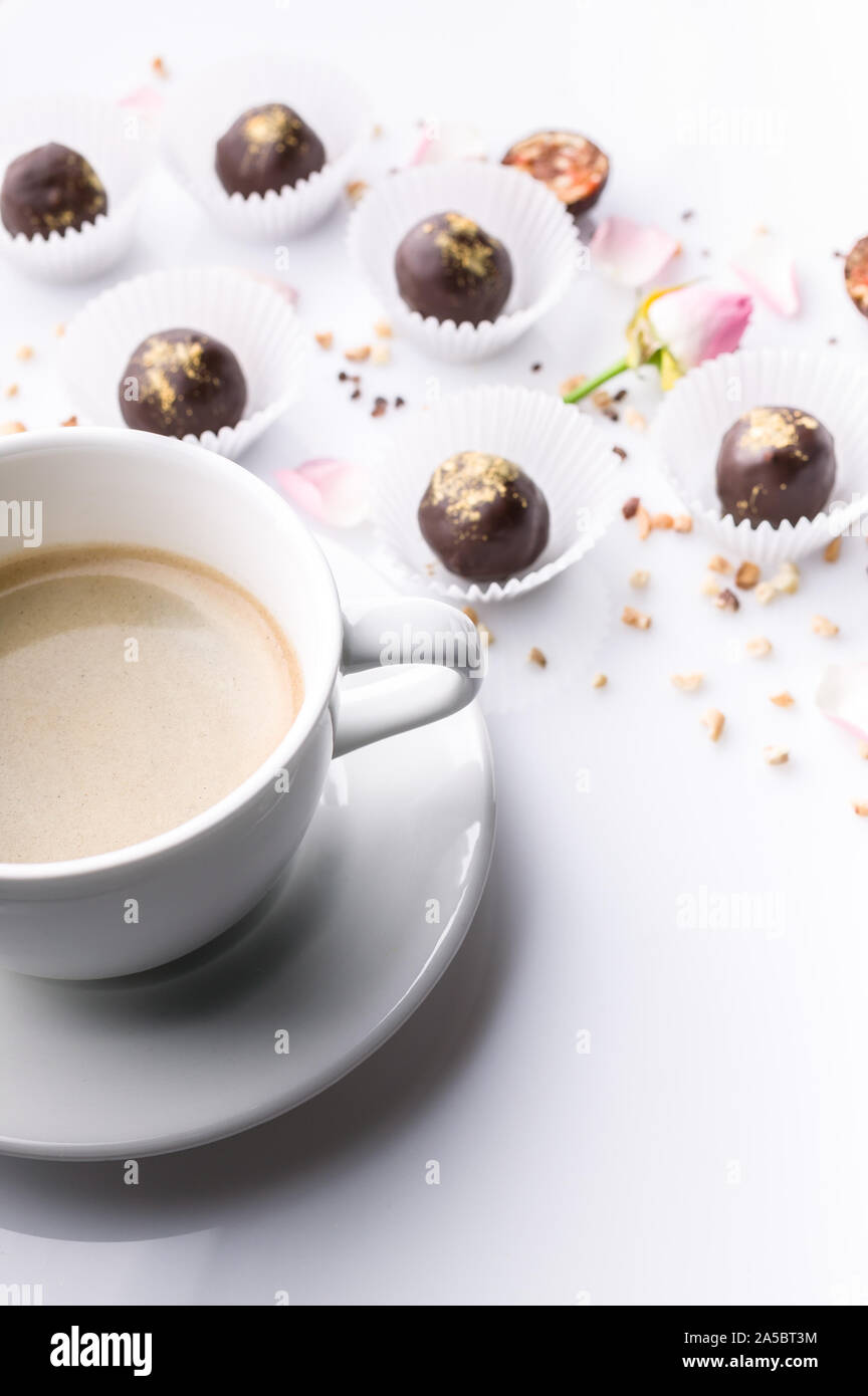 Bianco di ceramica tazza di caffè e cioccolatini fatti a mano con i dadi su uno sfondo bianco. Colpo verticale Foto Stock
