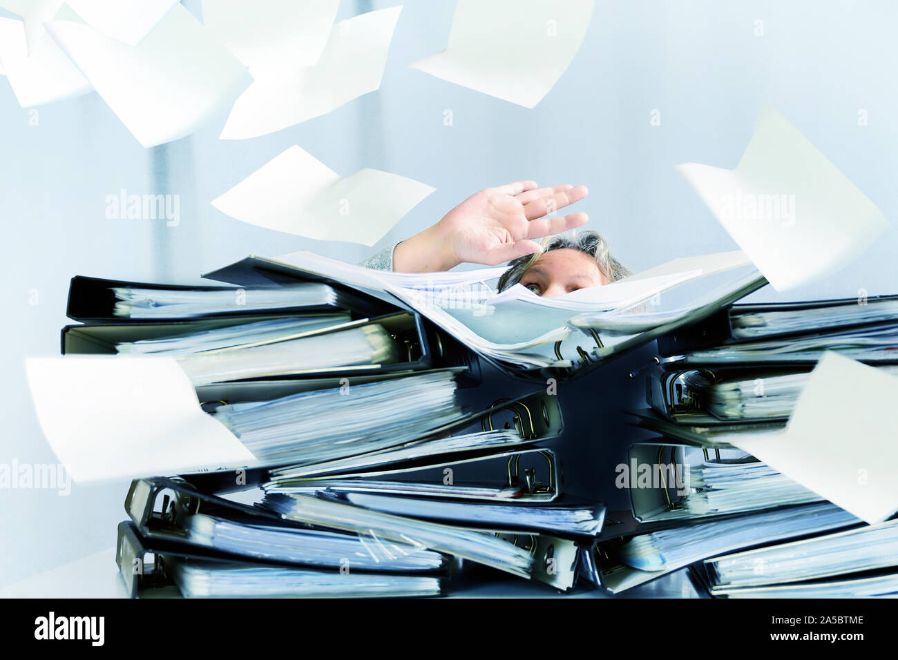 Donna disperata dietro alte pile di classificatori e un sacco di carte sono battenti in giro per l'ufficio, il concetto di richieste eccessive e aumentare wor Foto Stock