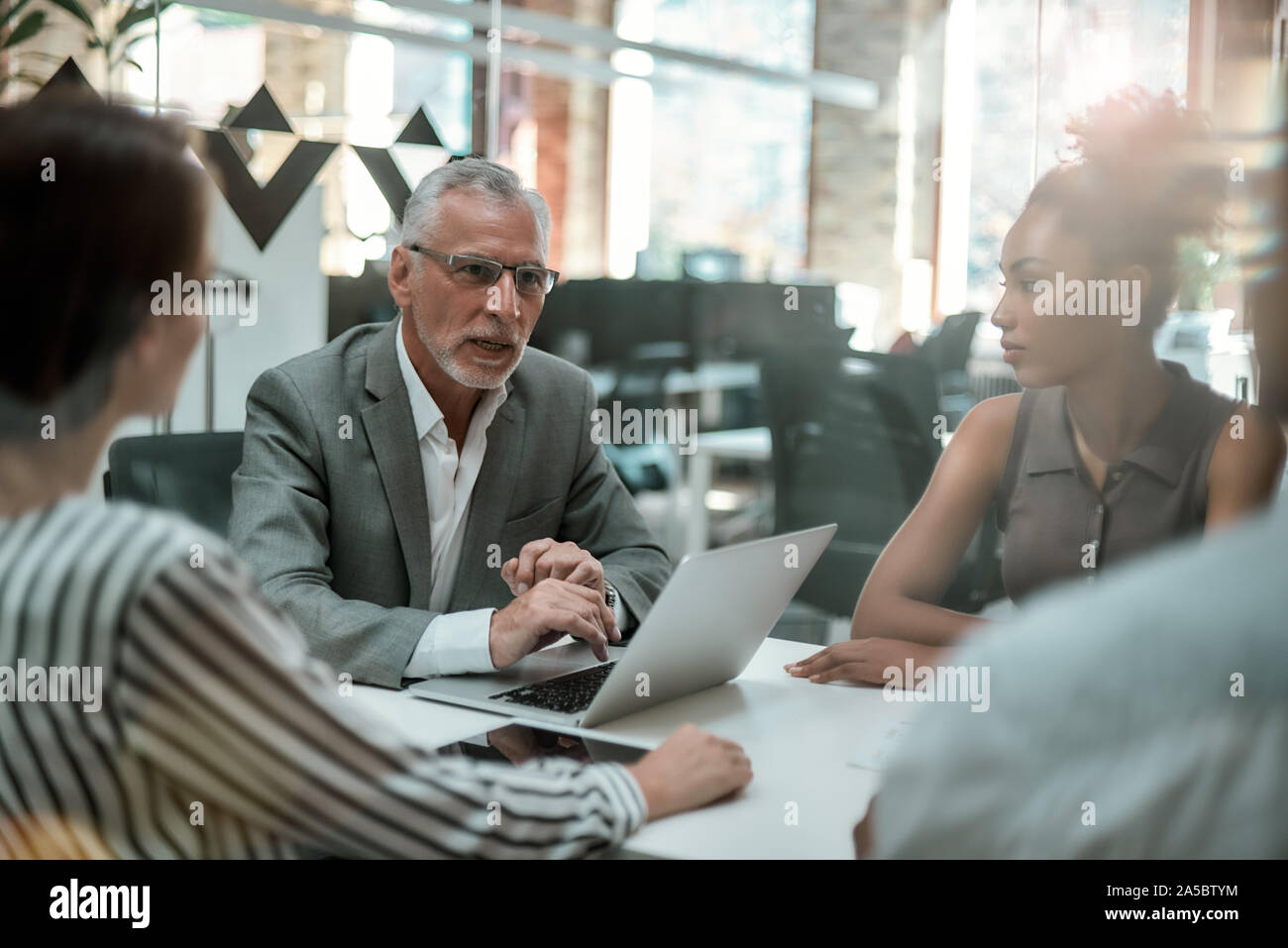 Il brainstorming. Grave uomo maturo in abbigliamento formale a discutere di qualcosa con il suo team multiculturale mentre è seduto al tavolo di office Foto Stock