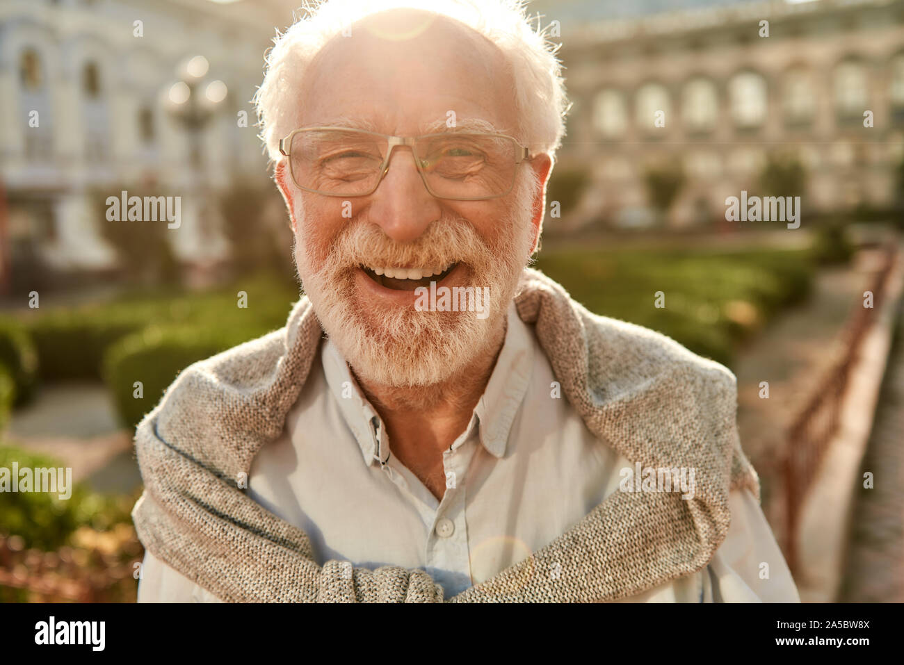 Età è solo un numero. Ritratto di felice e bello uomo senior in bicchieri guardando la fotocamera e sorridere mentre in piedi all'aperto in una giornata di sole Foto Stock
