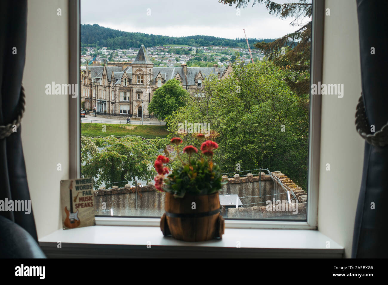 Guardando fuori una finestra di hotel a Inverness, Scotland. Un impianto di POT si siede sul davanzale, mentre altri edifici dal 1870 sono visibili in background Foto Stock
