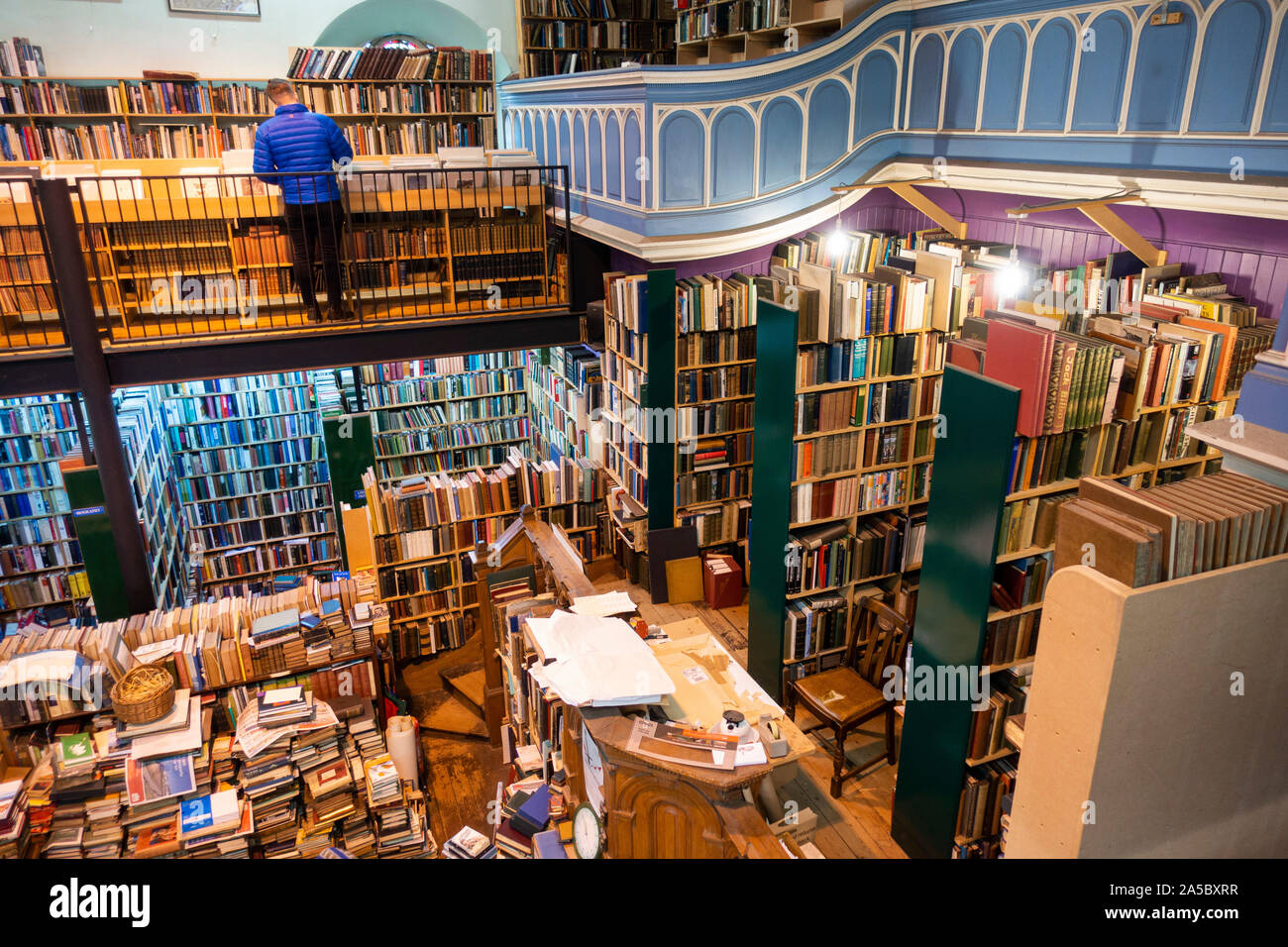 Un turista accede ripiani a Leakey's Bookshop, dotate di una vasta collezione di libri di seconda mano, esteso su due piani a Inverness, Scotland Foto Stock