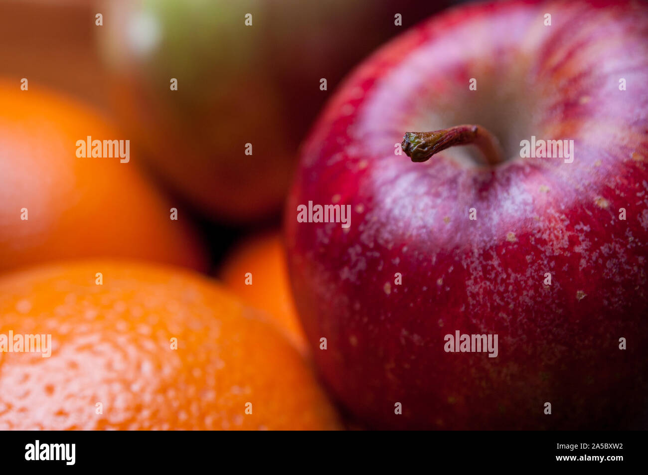 Lo stelo di una mela Red Delicious mantiene la messa a fuoco in questo close-up di mele e arance. Foto Stock