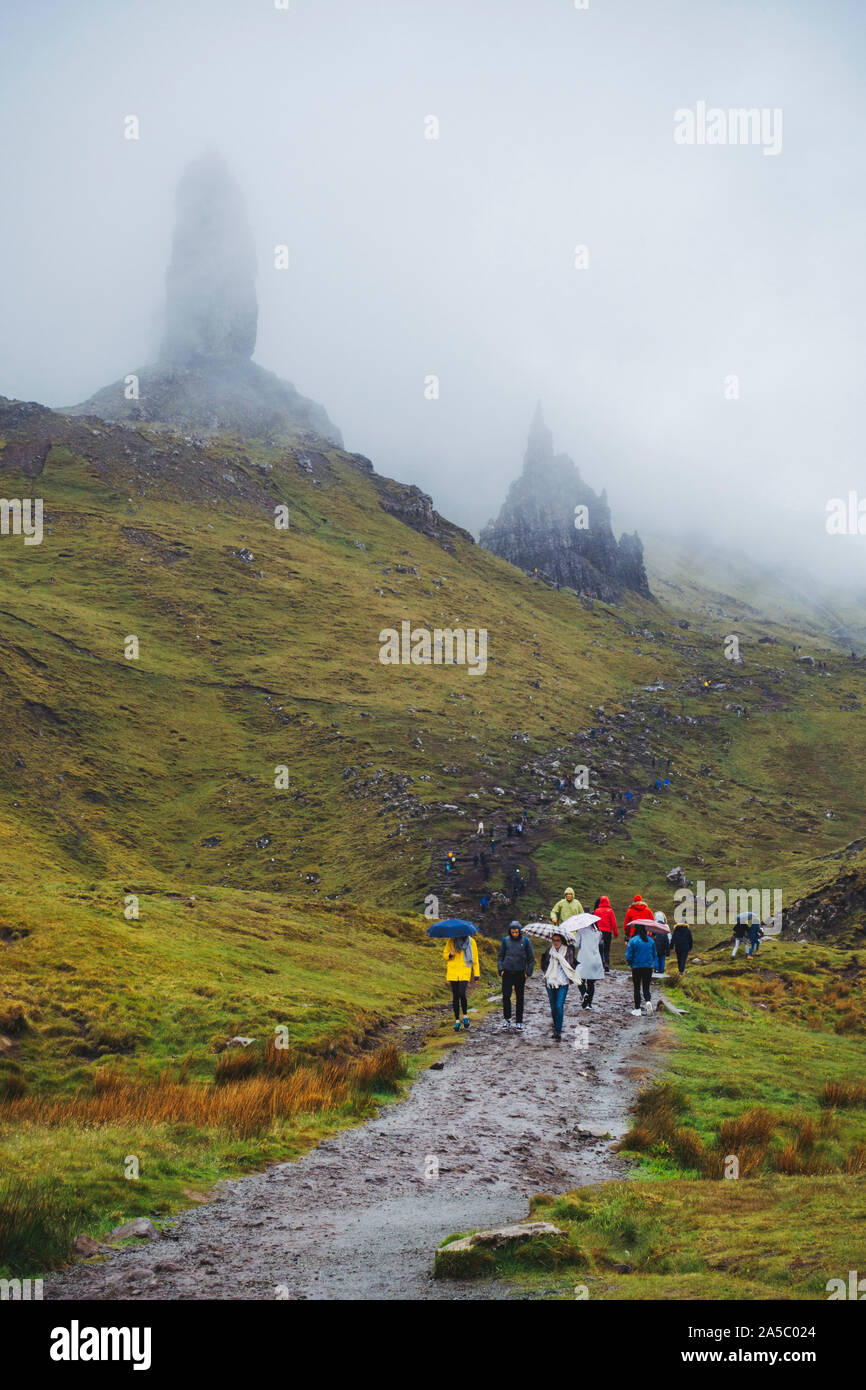 I turisti don impermeabili e ombrelloni in una piovosa, nuvoloso giorno presso il vecchio uomo di Storr, una famosa formazione rocciosa sull'Isola di Skye in Scozia Foto Stock