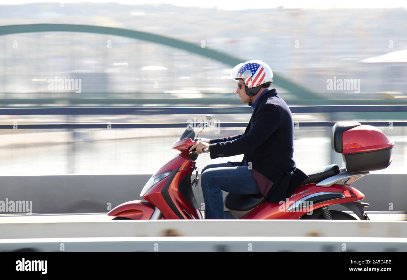A Belgrado, in Serbia - Ottobre 16, 2019: un uomo in blazer e jeans che indossa bandiera americana di equitazione casco scooter rossa sopra la città street bridge in occupato Foto Stock