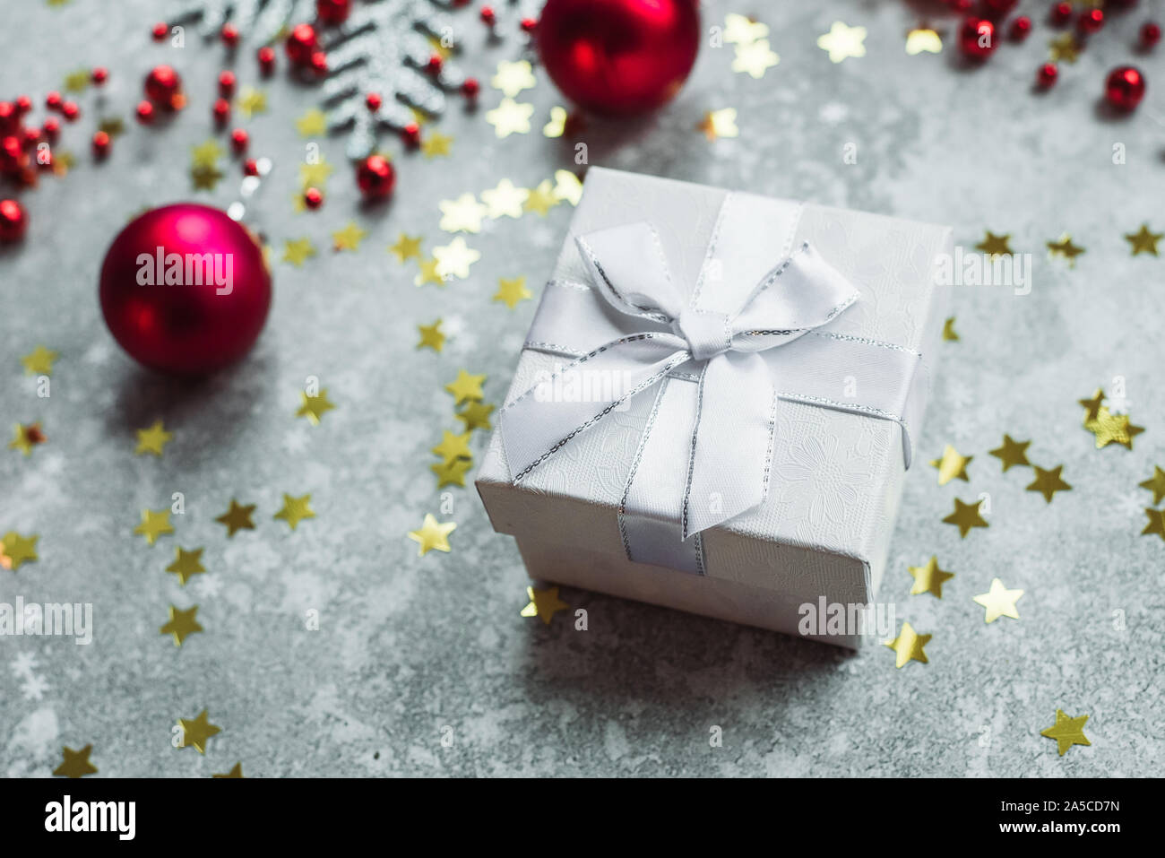 Argento regalo con fiocco sul grigio sfondo innevato con rosso palle di Natale e oro coriandoli stelle. Foto Stock