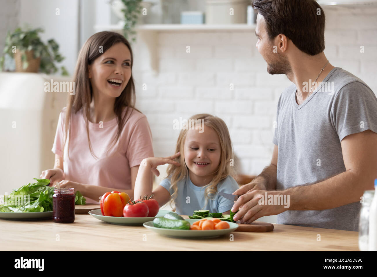 La famiglia felice con la piccola figlia la preparazione di insalate per la cena insieme Foto Stock