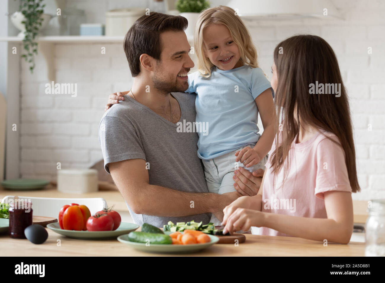 Padre sorridente azienda piccola figlia, famiglia prepara la cena in cucina Foto Stock