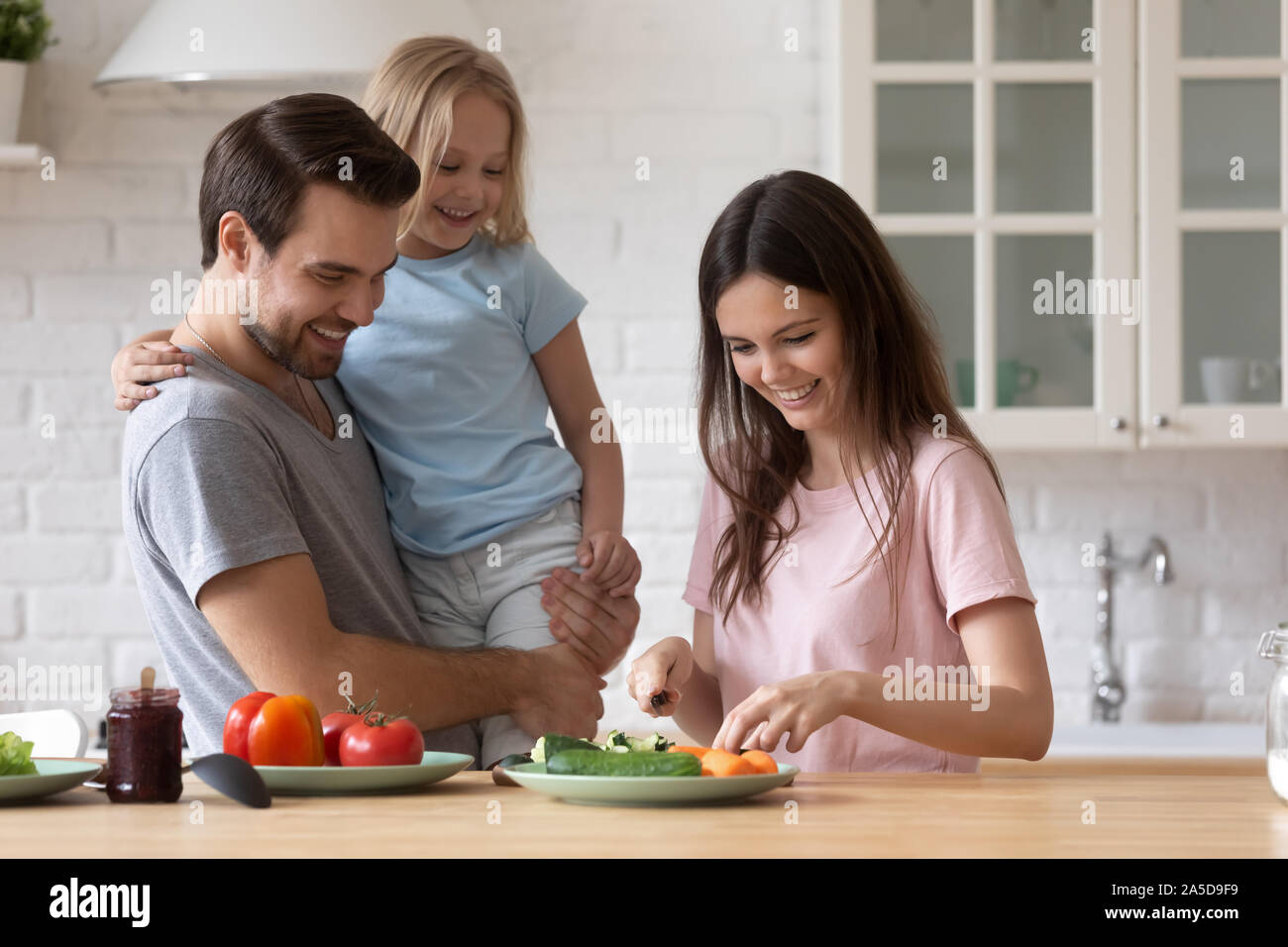 Felice padre e figlia piccola guardando madre insalata di cottura Foto Stock