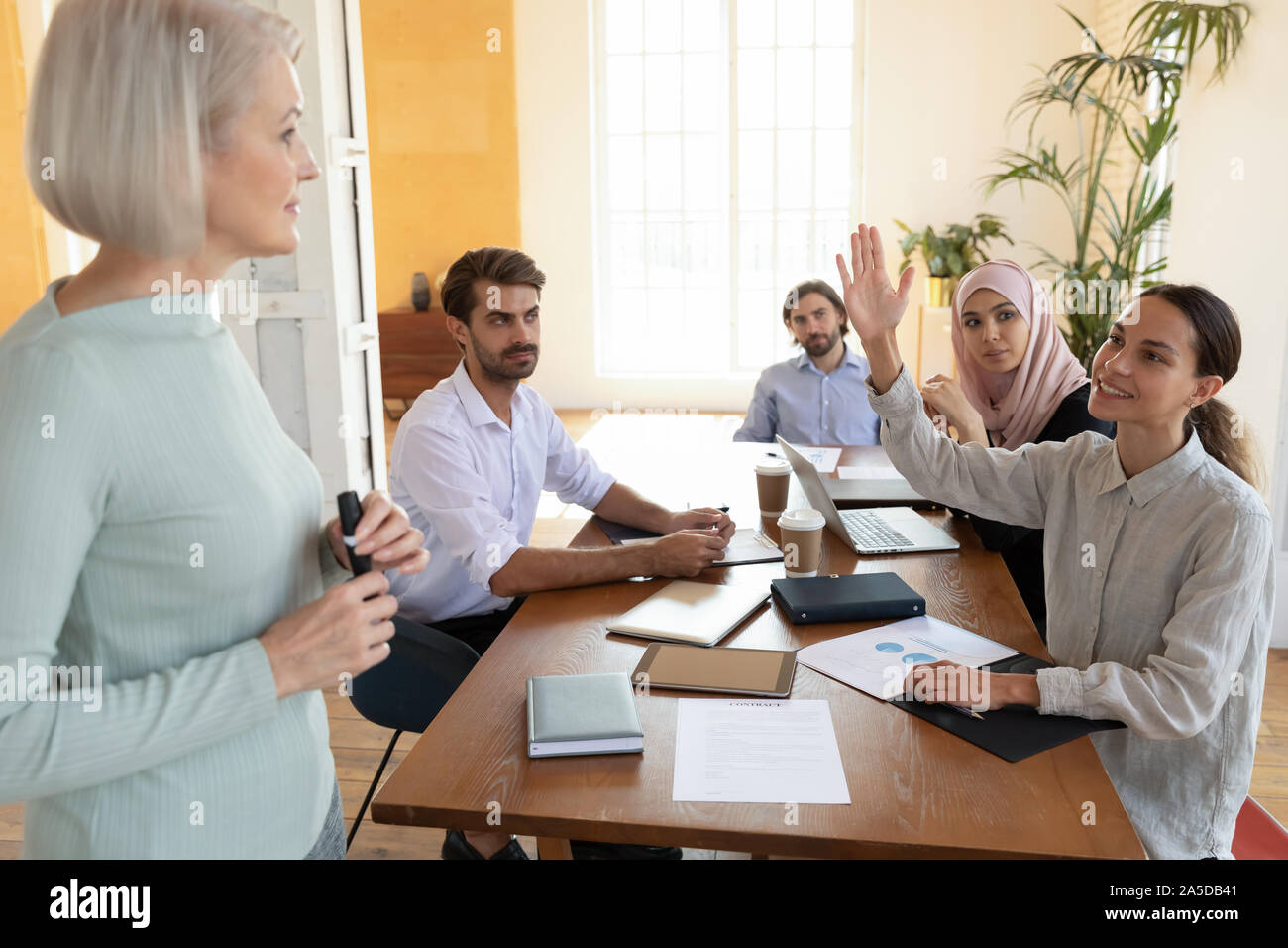 Giovane imprenditrice del partecipante al corso di formazione di alzare la mano chiedere al vecchio mentore domanda Foto Stock