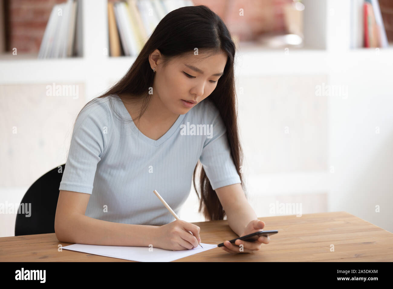 Studente vietnamita utilizzando app scaricate sul telefono studiando seduto al chiuso Foto Stock