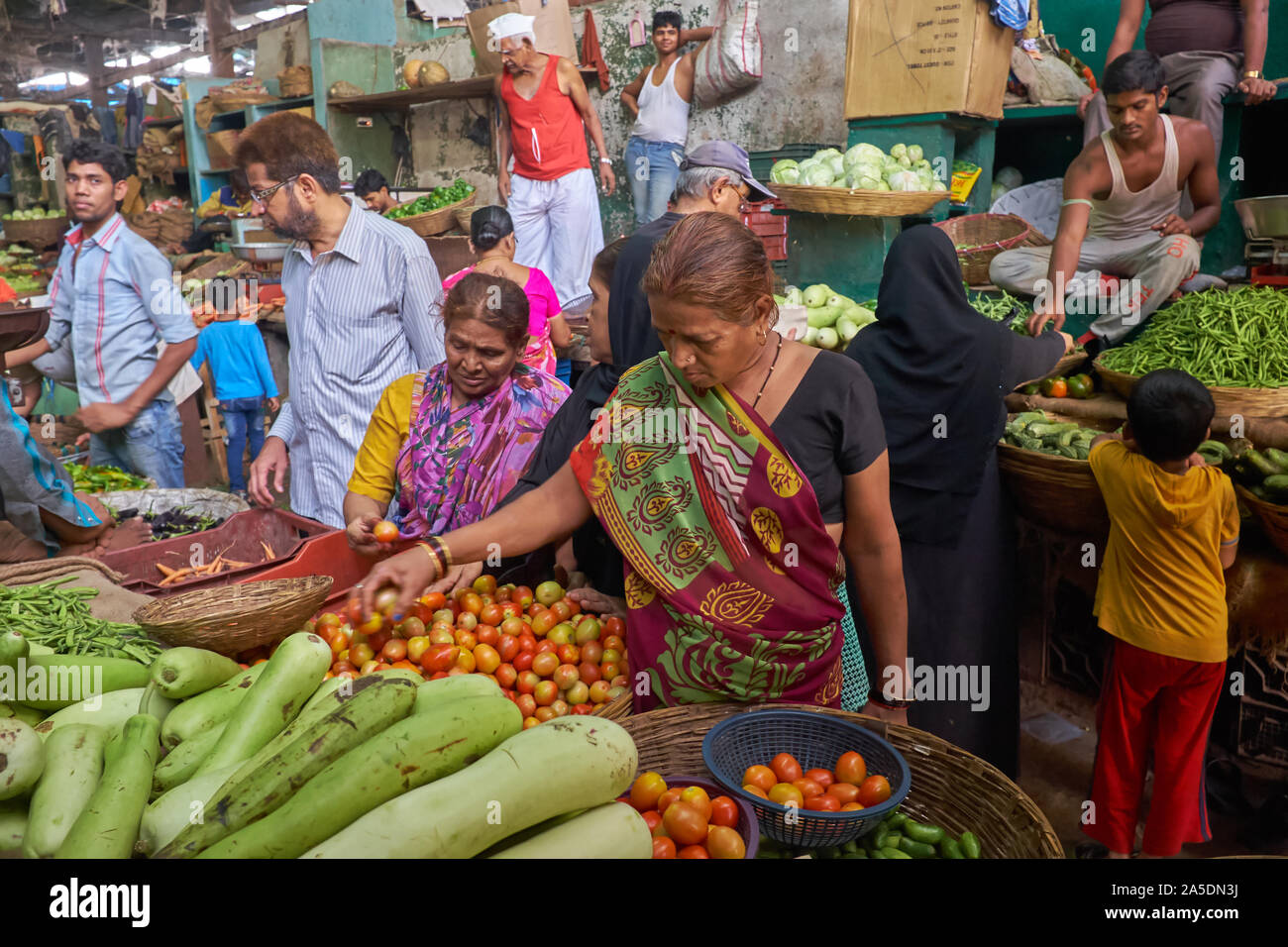 In un mercato ortofrutticolo nel centro di Mumbai, India, una casalinga scruta alcune verdure con segnale di occupato delle attività di mercato tutti intorno a lei Foto Stock