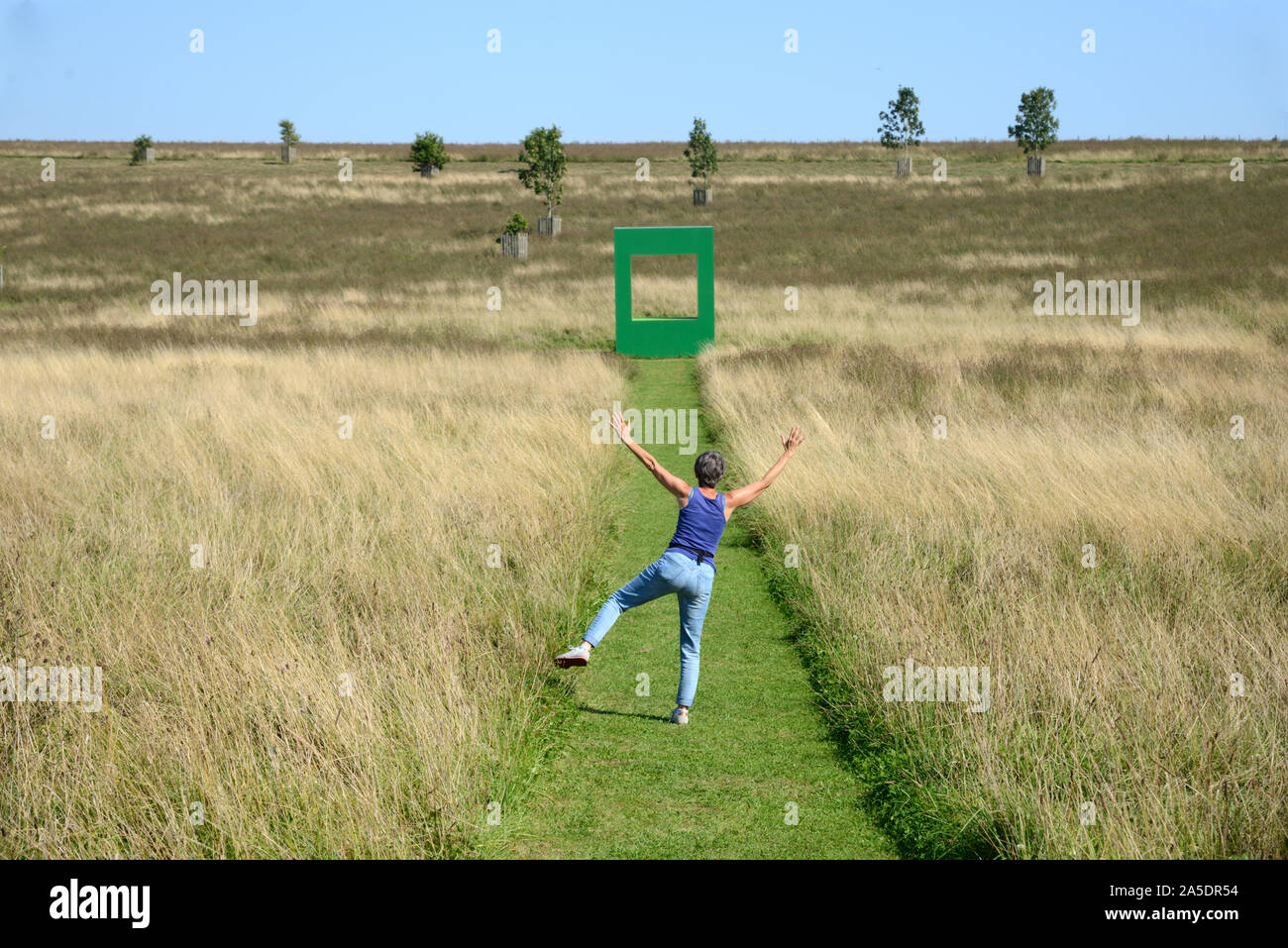 Donna europea ingannare circa su erba falciata in campo verde con abitazione installazione d arte da Krijn de Koning 2019 in background Compton Verney Inghilterra Foto Stock