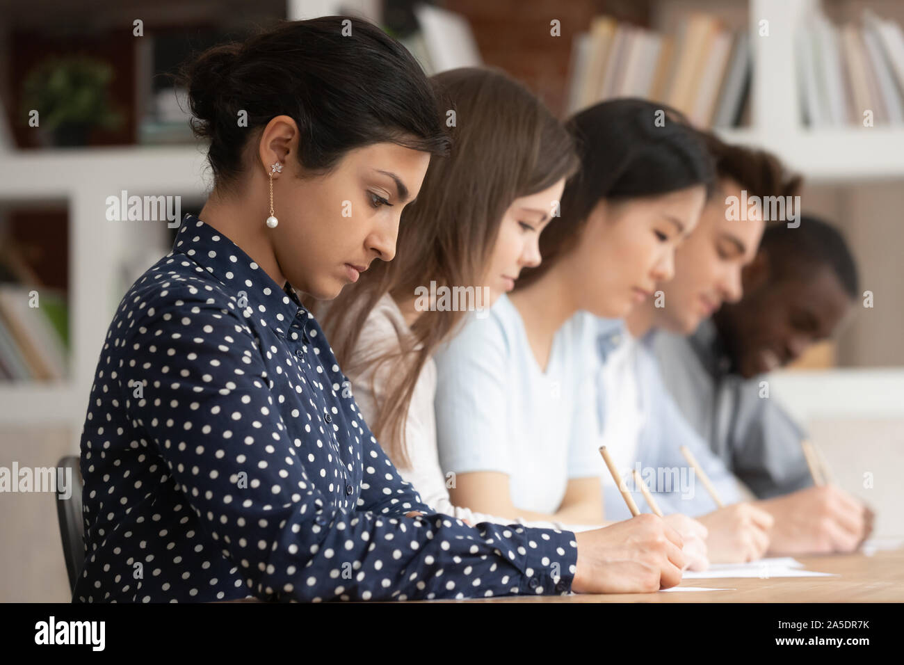 Multirazziale studenti seduti alla scrivania la scrittura su carte facendo task Foto Stock