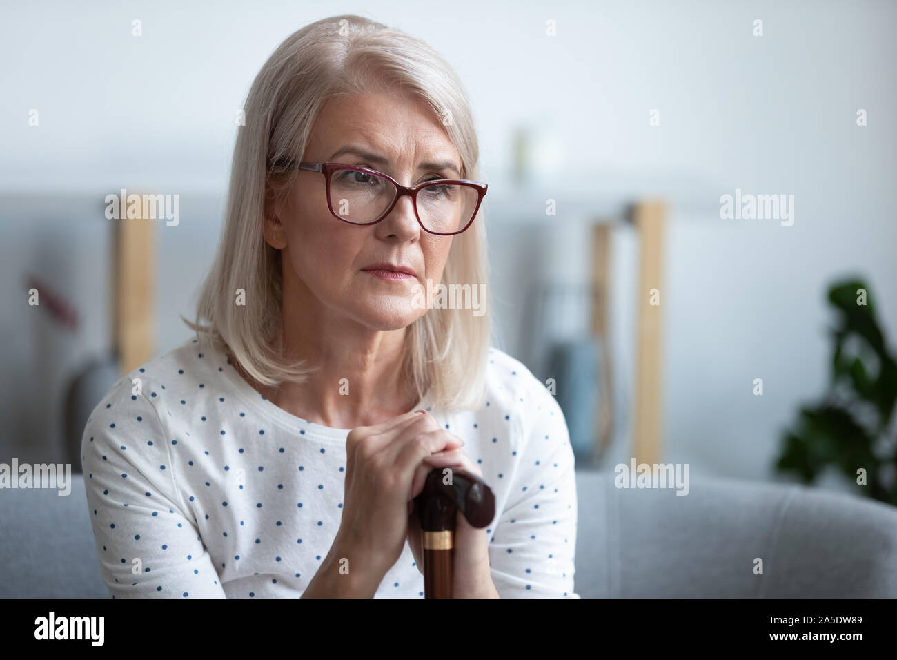 Triste lonely premurosa donna vecchia tenendo la canna da zucchero sedersi a casa Foto Stock