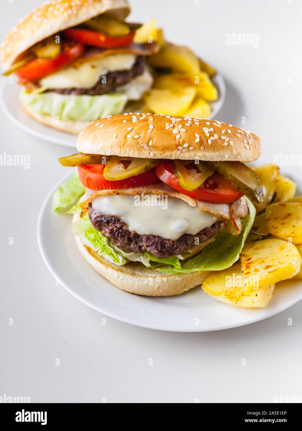 Due hamburger fatti in casa con una succosa carne cotoletta, parmigiano, insalata verde, pomodori e patate fritte su uno sfondo luminoso. Colpo verticale Foto Stock