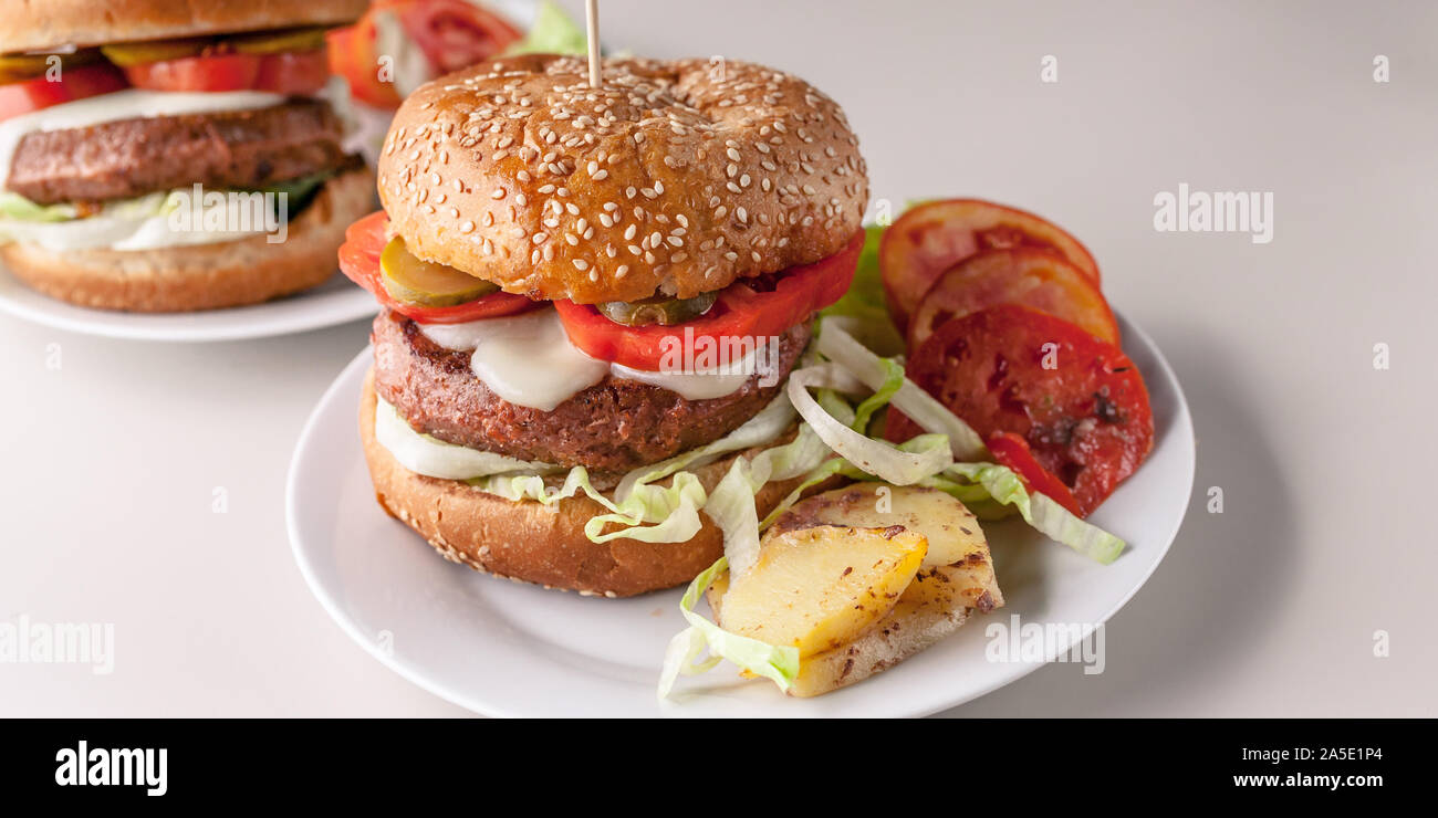 Cibo banner: due hamburger fatti in casa con una succosa carne cotoletta, parmigiano, insalata verde, pomodori e patate fritte su uno sfondo luminoso. Foto Stock