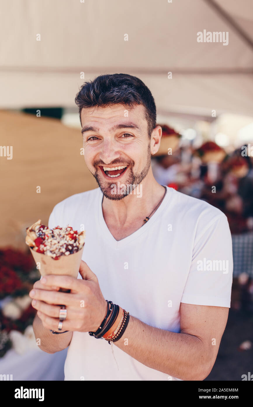 Felice giovane uomo caucasico holding waffle e ridere sul festival Foto Stock