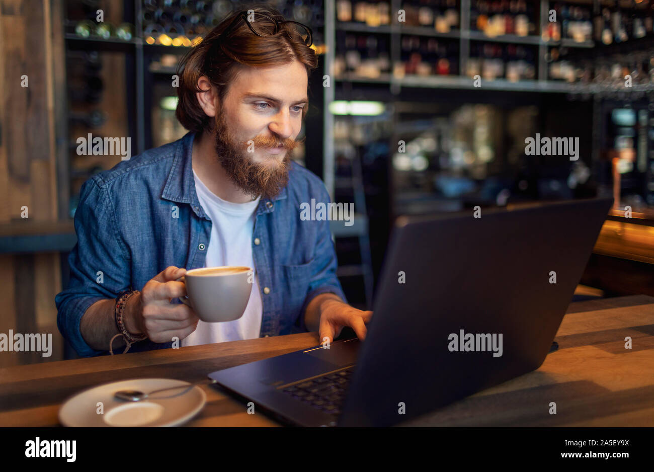 Giovani barbuto freelancer per controllare la posta elettronica tramite computer portatile mentre avente il caffè di mattina in un loft bar Foto Stock