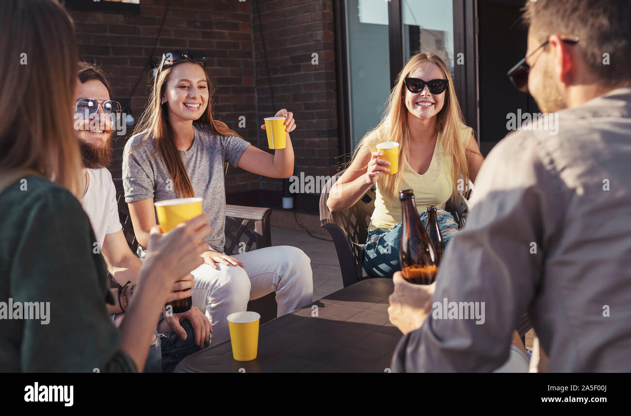 Ragazza carina alza il suo bicchiere durante un venerdì di amici su una terrazza al tramonto Foto Stock