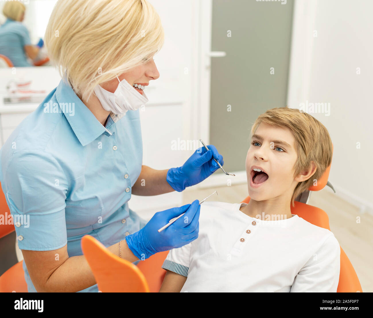 Attenzione dentista donna esaminando boy i denti con una bocca a specchio e una sonda Foto Stock