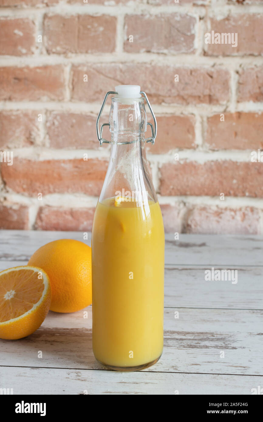 Spremuta di arancia fresca in piedi sul tavolo di legno su un muro di mattoni sfondo con arance fresche. Una sana detox bevanda. Foto Stock