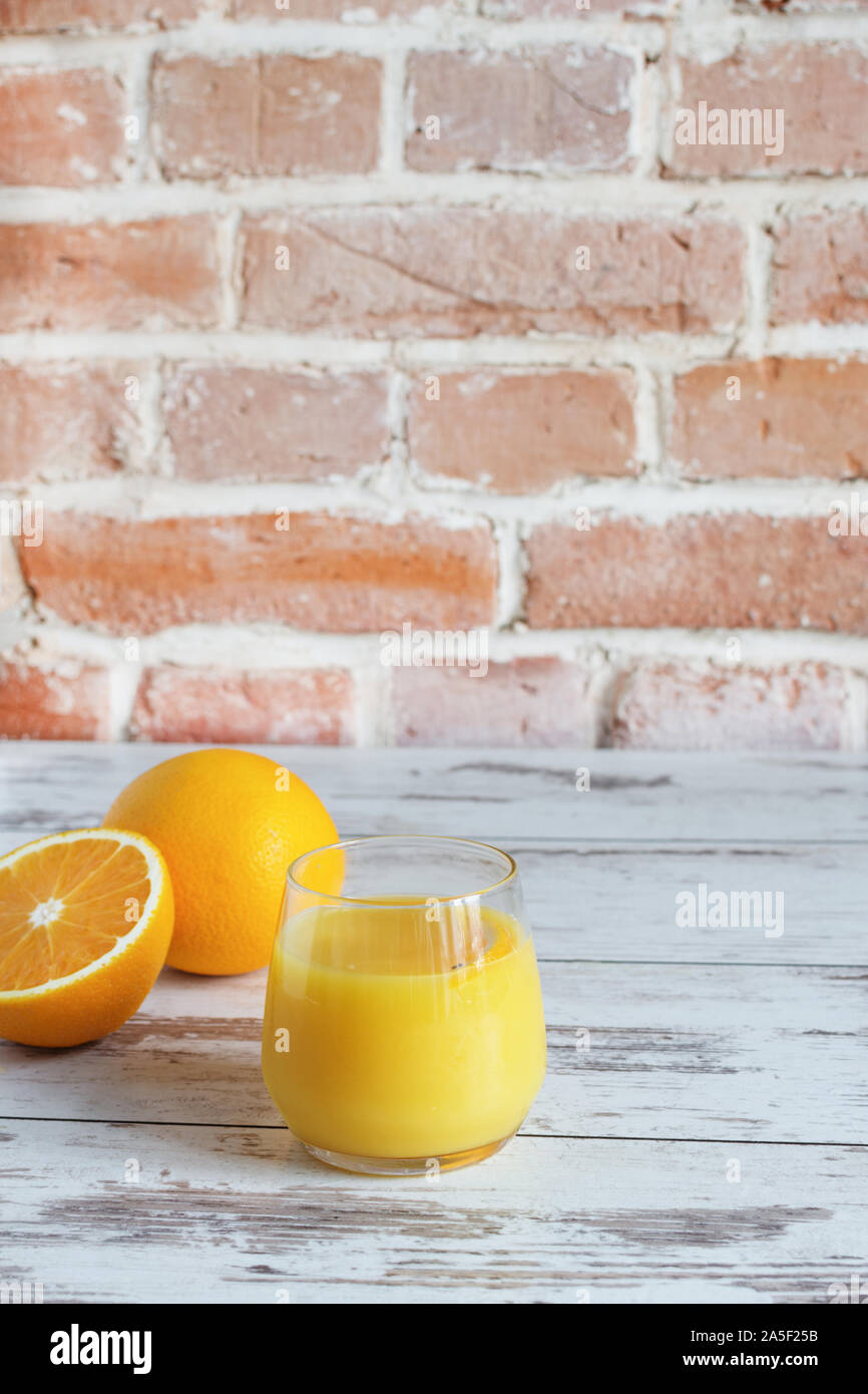 Spremuta di arancia fresca in piedi sul tavolo di legno su un muro di mattoni sfondo con arance fresche. Una sana detox bevanda. Foto Stock