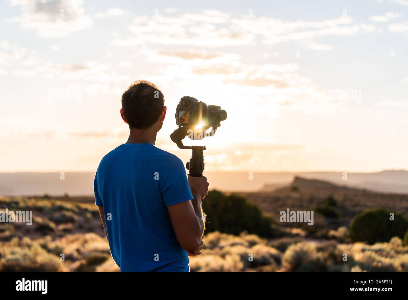 Uomo con sospensione cardanica fotocamera stabilizzatore riprese con sunrise sunburst flare attraverso apparecchiature nel Parco Nazionale di Arches, Utah a fornace ardente Viewpoint Foto Stock