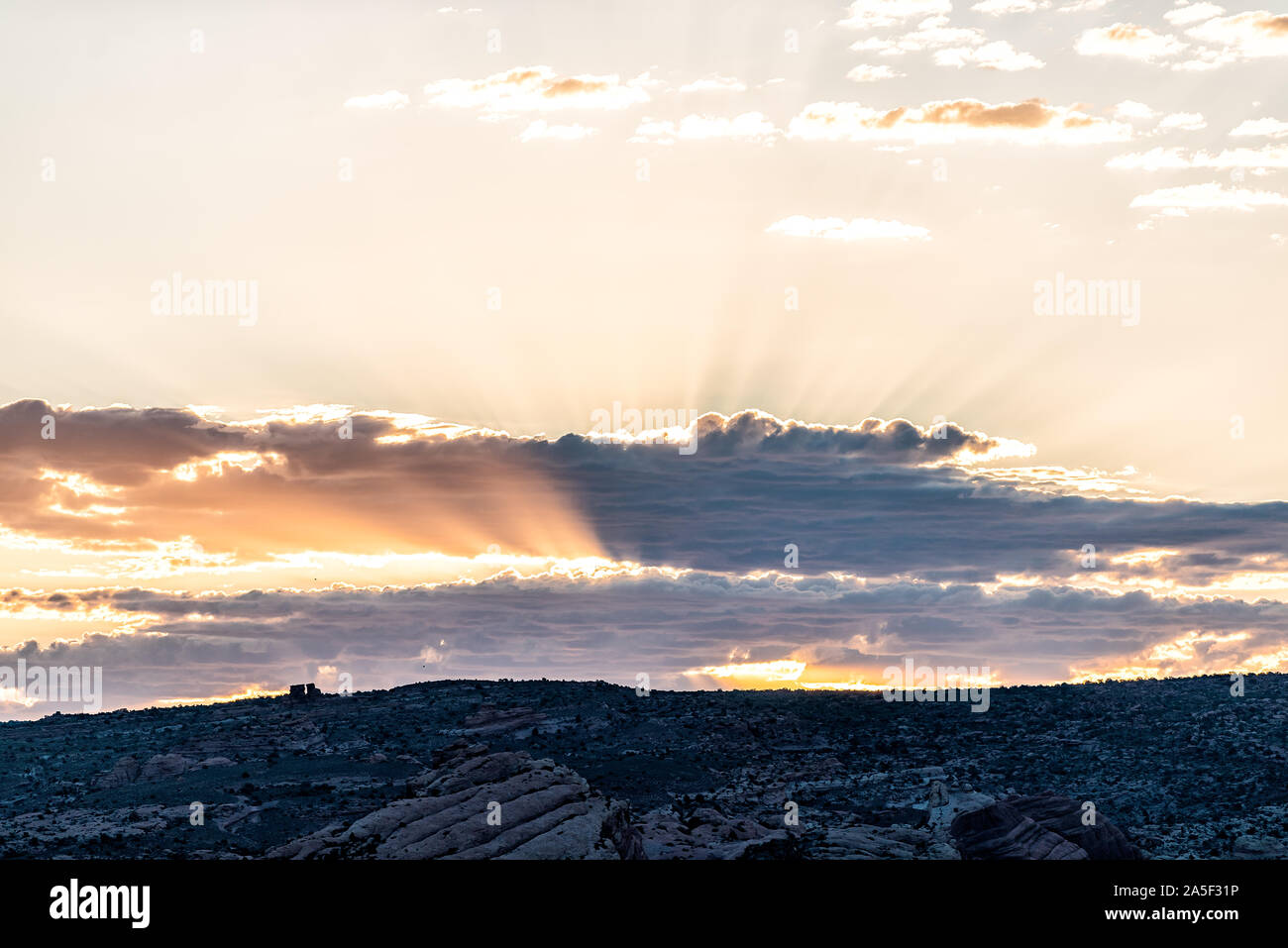 Vista del paesaggio di alba con il sole che tramonta dietro le nuvole e la luce del sole fasci di raggi attraverso il cielo con orizzonte valley nel Parco Nazionale di Arches, Utah, Stati Uniti d'America Foto Stock