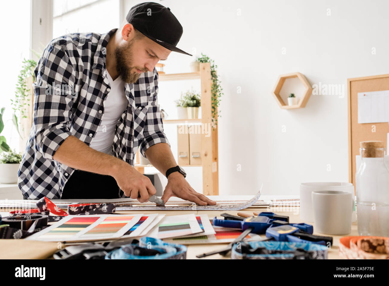 Giovane uomo creativo in informale di piegarsi sul luogo di lavoro durante la preparazione di pezzi in lavorazione decorativa per collari di pet in studio Foto Stock