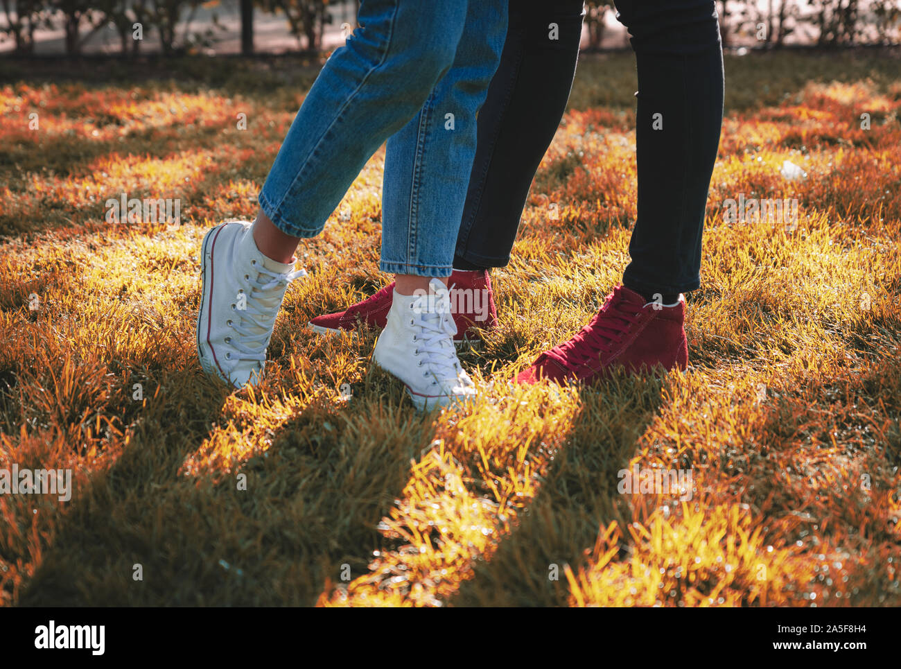 Maschio e femmina di gambe in sneakers e jeans. Nella parte anteriore di ogni altro sulla colorata caduto erba, vista laterale. Moda casual selfie, autunno amore concetto. Foto Stock