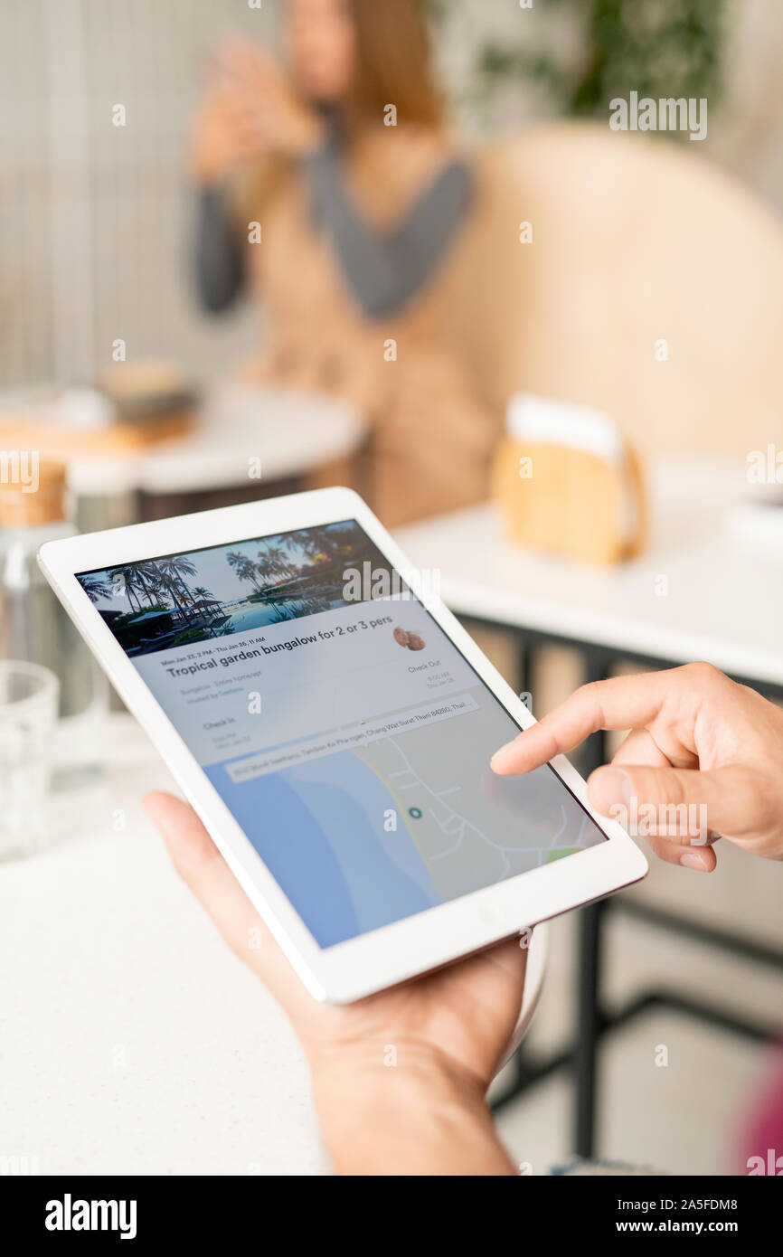 La mano del giovane uomo puntando al tablet schermo durante la ricerca sul sito web per i viaggiatori e la scelta di tour Foto Stock