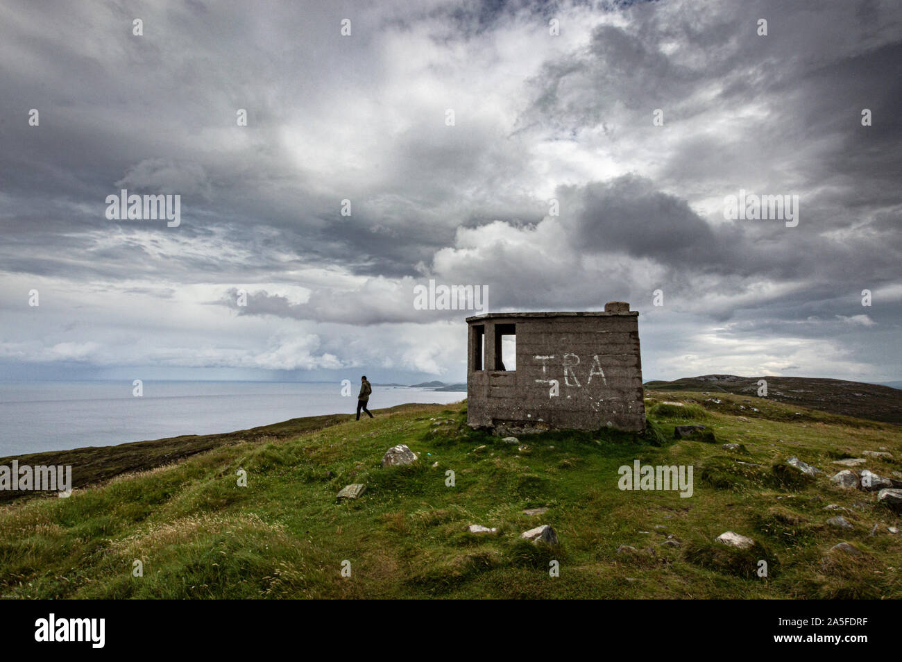 Un viandante lascia un posto di vedetta affacciato sull'Oceano Atlantico sulla Costa di Donegal, Irlanda con fading grafitti IRA Foto Stock