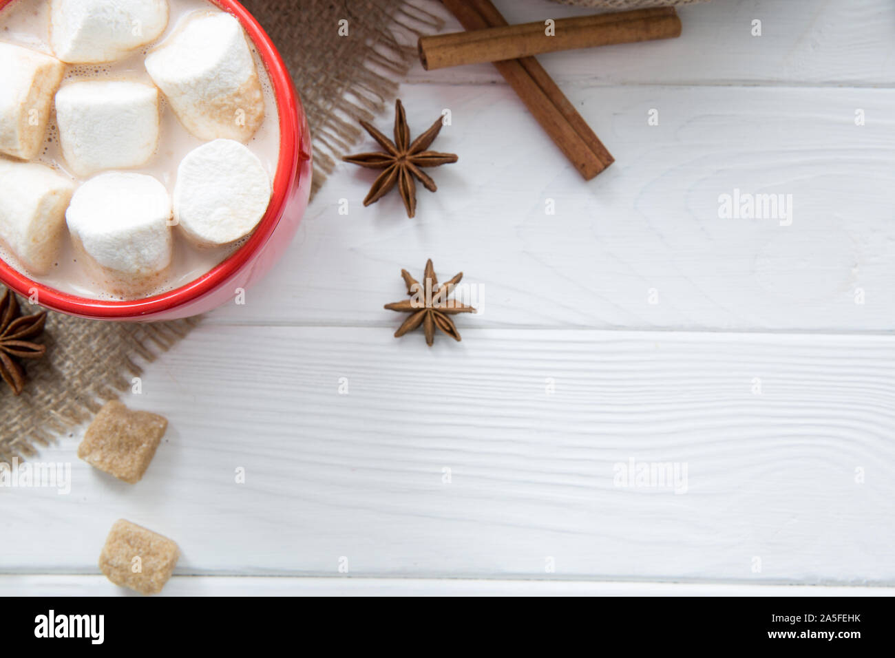 Natale rosso con tazza di cioccolata calda e marshmallow. Cioccolata calda con latte, anice e cannella rotoli su legno bianco sfondo rustico, hessian (sackin Foto Stock