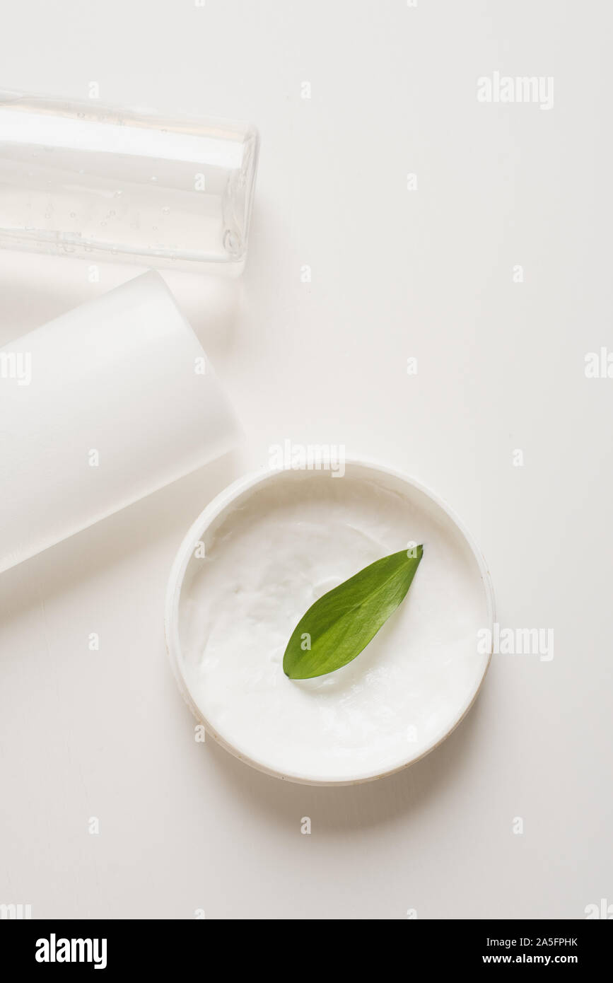 Mezzi per la cura della pelle, ringiovanimento e idratazione del viso. Crema di latte, acqua micellare e lozione idratante su uno sfondo bianco con una foglia verde. Il concetto di self-care e cura per la pelle. Foto Stock