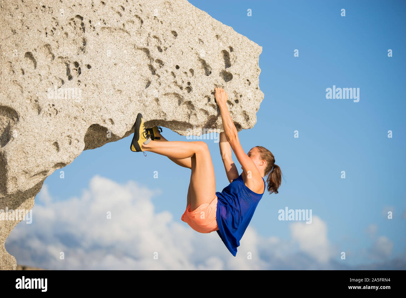Donna arrampicata sul masso naturale di roccia alla spiaggia, Corsica, Francia Foto Stock