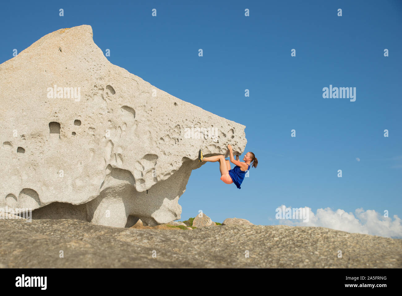 Donna arrampicata sul masso naturale di roccia alla spiaggia, Corsica, Francia Foto Stock