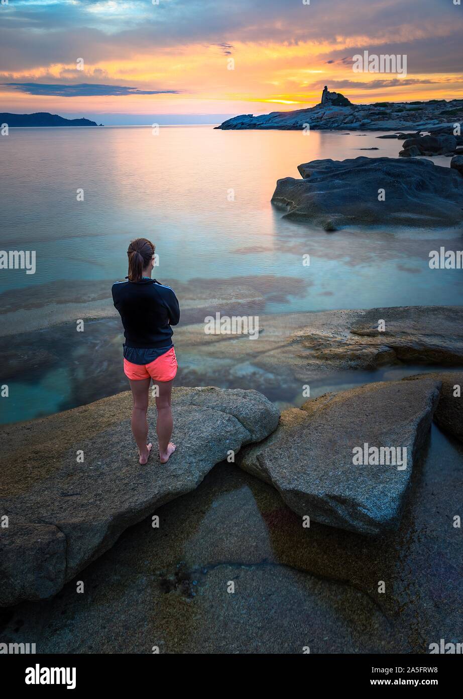 Donna in piedi sulla spiaggia guardando a vista al tramonto, Corsica, Francia Foto Stock