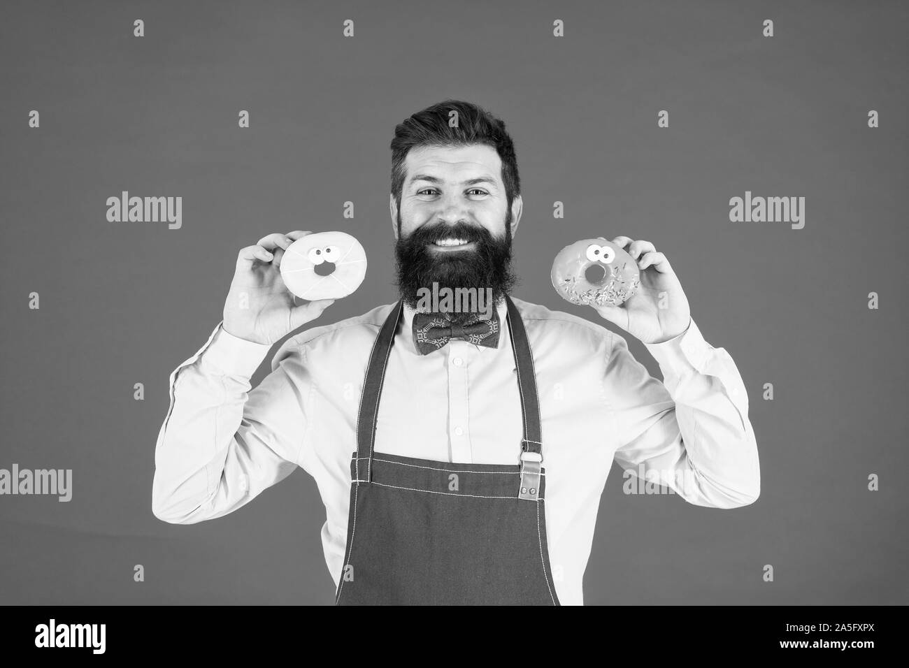 Bakery business. Beni cotti al forno. Dolci e Torte. Il cibo spazzatura. Hipster barbuto baker tenere ciambelle. Ciambella panificio. Ciambella di vetrate. Barbuto allegro ben curato uomo in grembiule ciambelle di vendita. Panificio proprietario. Foto Stock